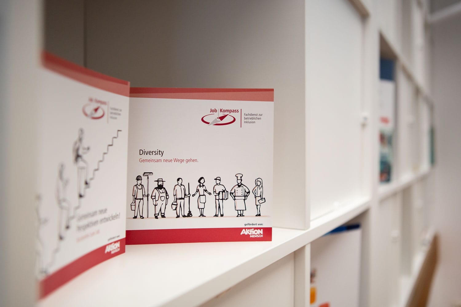 Flyer des JobKompass von Alexianer 360 Grad Ein Flyer über den JobKompass der Alexianer Werkstätten in einem Regal