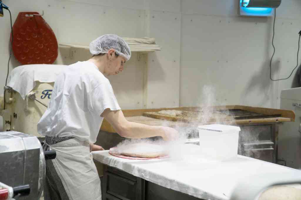Ein Mitarbeiter streut Mehl auf eine Arbeitsfläche.
